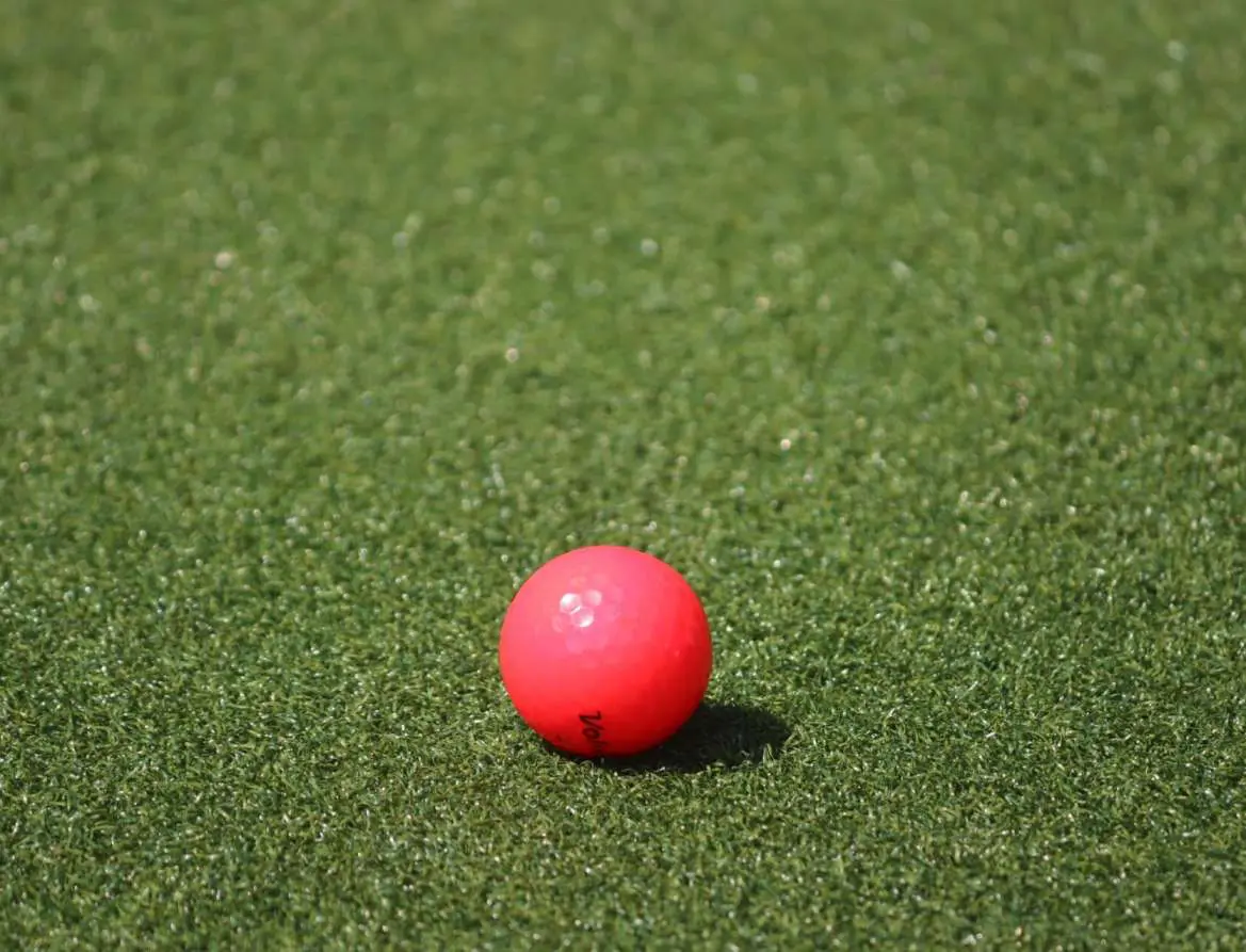 A close-up of a bright pink ball resting on a well-trimmed artificial turf surface. The ball appears slightly textured and is placed centrally in the image, evoking memories of vibrant playing fields.