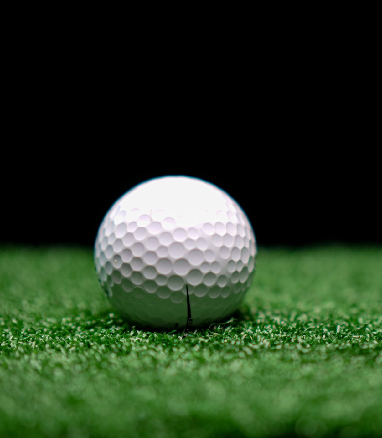 A close-up image of a golf ball with a crack in it, sitting on quality putting greens against a plain black background. The ball is centered and the textured surface of the turf, expertly laid by artificial putting green installers, is clearly visible.