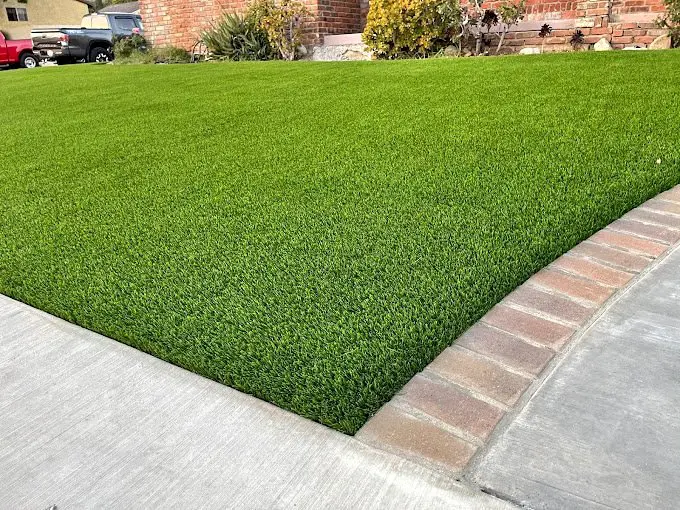 a close up of some artificial grass for pets in chandler AZ. Showing the green synthetic grass next to a paver driveway. 